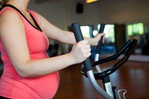 A pregnant woman doing cardiovascular exercise on a crosstrainer in a gym