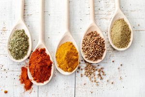 various spices in wooden spoons on old white wooden table