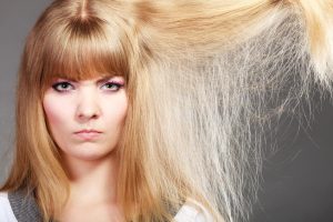 Haircare. Blonde woman with her damaged dry hair angry face expression gray background