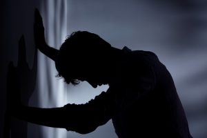 Man leaning with hands against wall, dark room